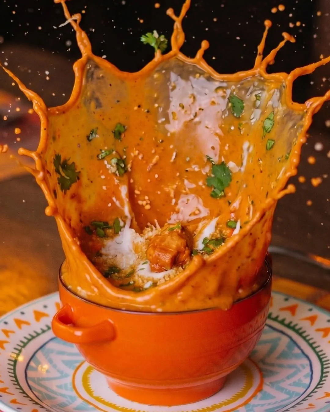Curry portocaliu care sare dintr-un vas emailat, pe o farfurie pictată