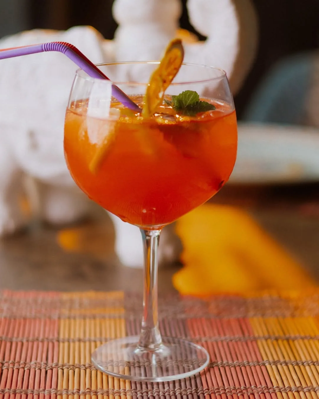 Cocktail portocaliu într-un pahar cu picior, lângă un elefant de porțelan