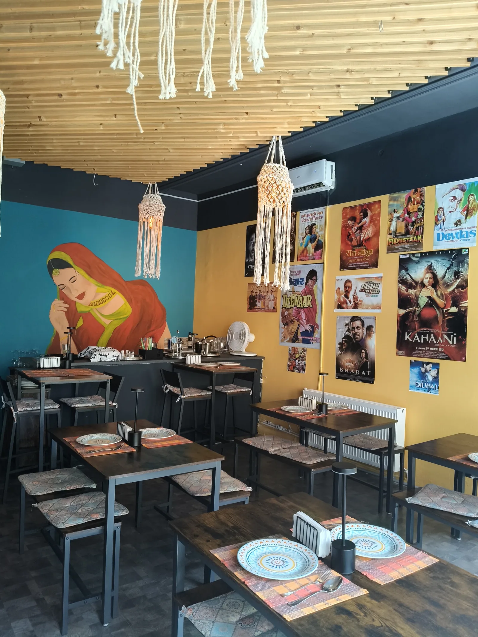Sala Soul: perete turcoaz cu o pictură murală, perete muștar cu afișe Bollywood și lămpi din macrameu